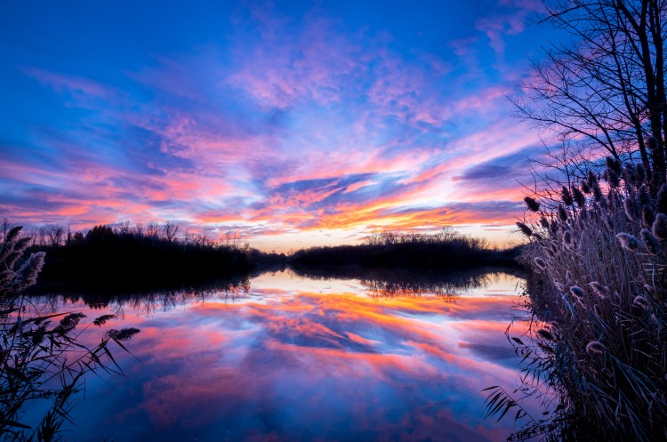 sunset, high clouds, deep blues, magentas and orange sunset reflecting in a perfectly calm lake
